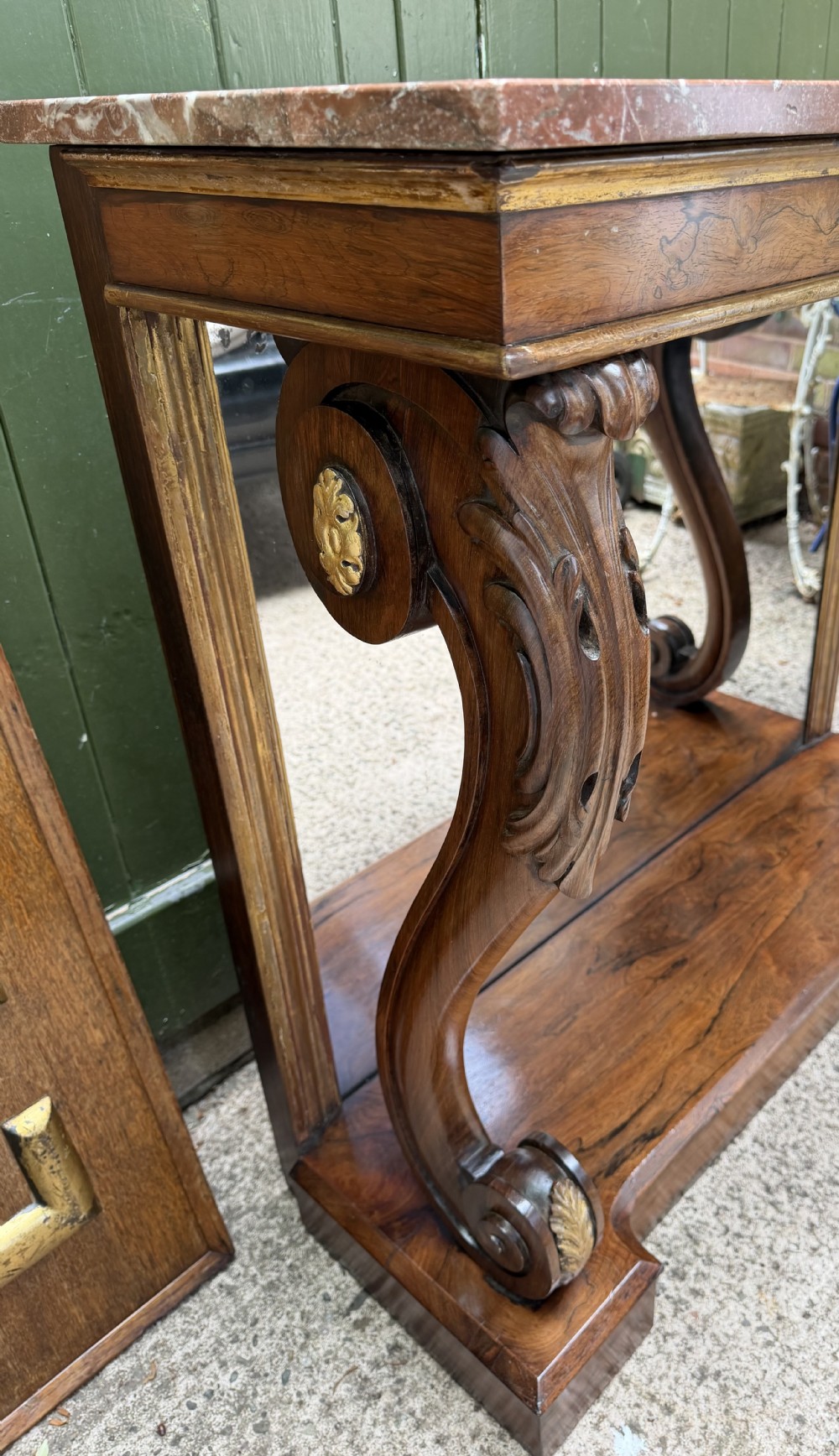 A Regency rosewood console table featuring a figured marble top, carved scroll legs with parcel-gilt details, an inset mirror back, and a plinth base. View XXII