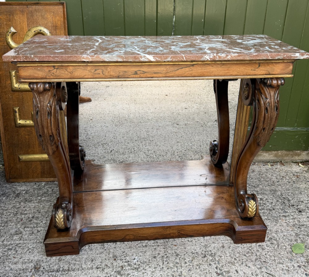 A Regency rosewood console table featuring a figured marble top, carved scroll legs with parcel-gilt details, an inset mirror back, and a plinth base. View XXIII
