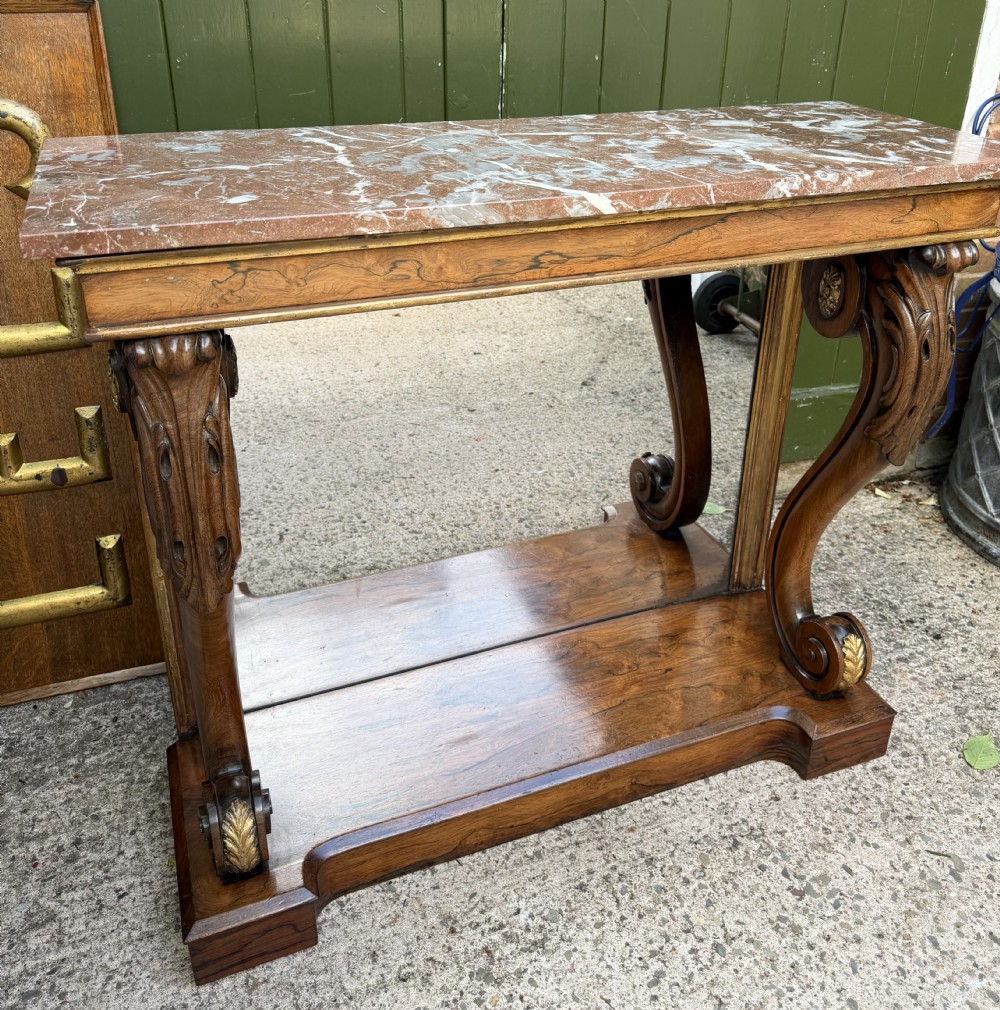 A Regency rosewood console table featuring a figured marble top, carved scroll legs with parcel-gilt details, an inset mirror back, and a plinth base. View XXIV