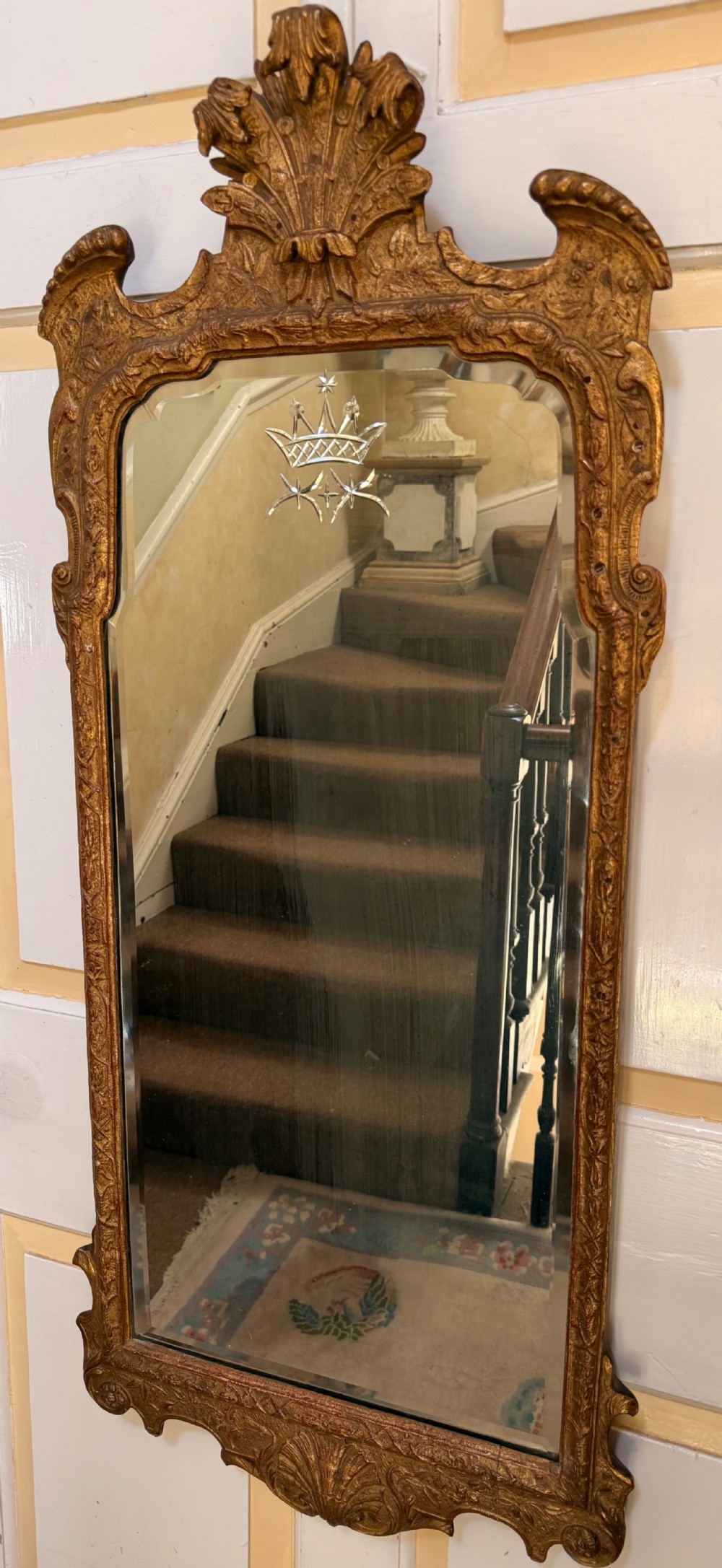 A tall, slender carved giltwood pier mirror featuring an ornate acanthus leaf cresting and an etched crest motif near the top of the glass plate.