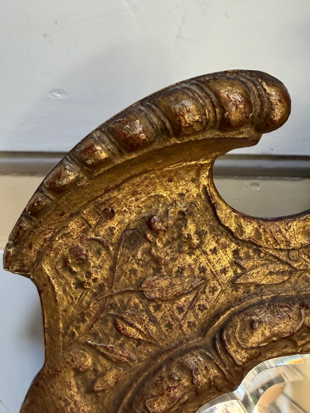 A tall, slender carved giltwood pier mirror featuring an ornate acanthus leaf cresting and an etched crest motif near the top of the glass plate. View V