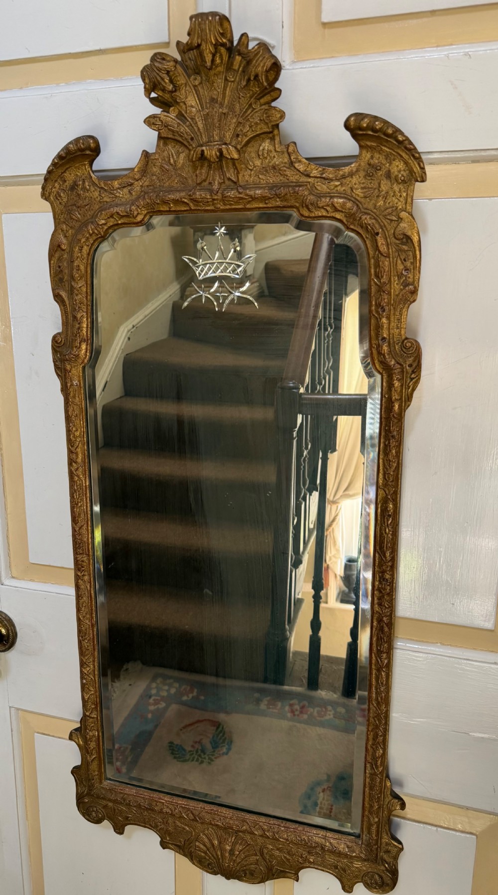 A tall, slender carved giltwood pier mirror featuring an ornate acanthus leaf cresting and an etched crest motif near the top of the glass plate. View IX