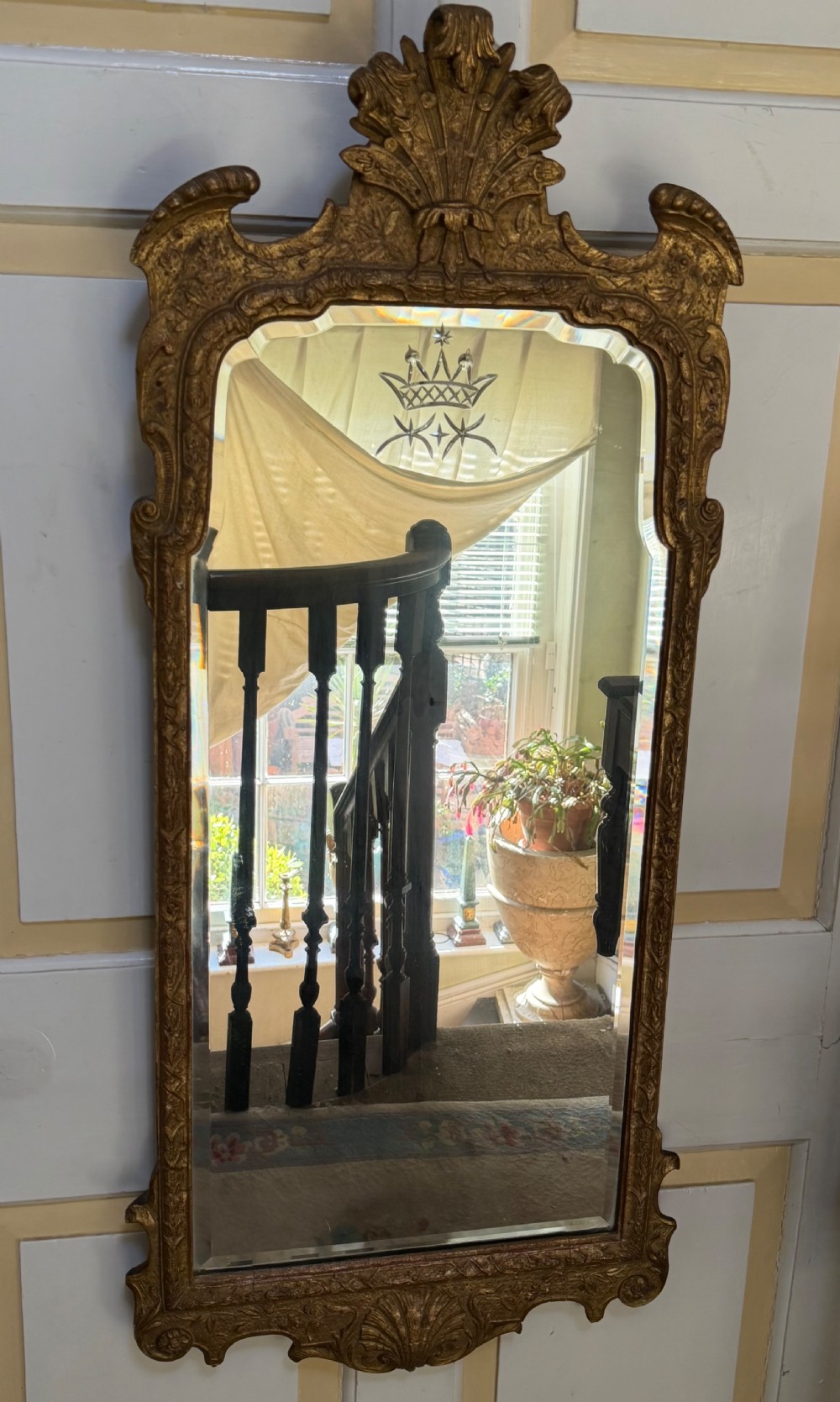 A tall, slender carved giltwood pier mirror featuring an ornate acanthus leaf cresting and an etched crest motif near the top of the glass plate. View X