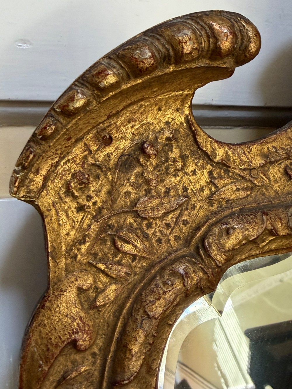 A tall, slender carved giltwood pier mirror featuring an ornate acanthus leaf cresting and an etched crest motif near the top of the glass plate. View XI