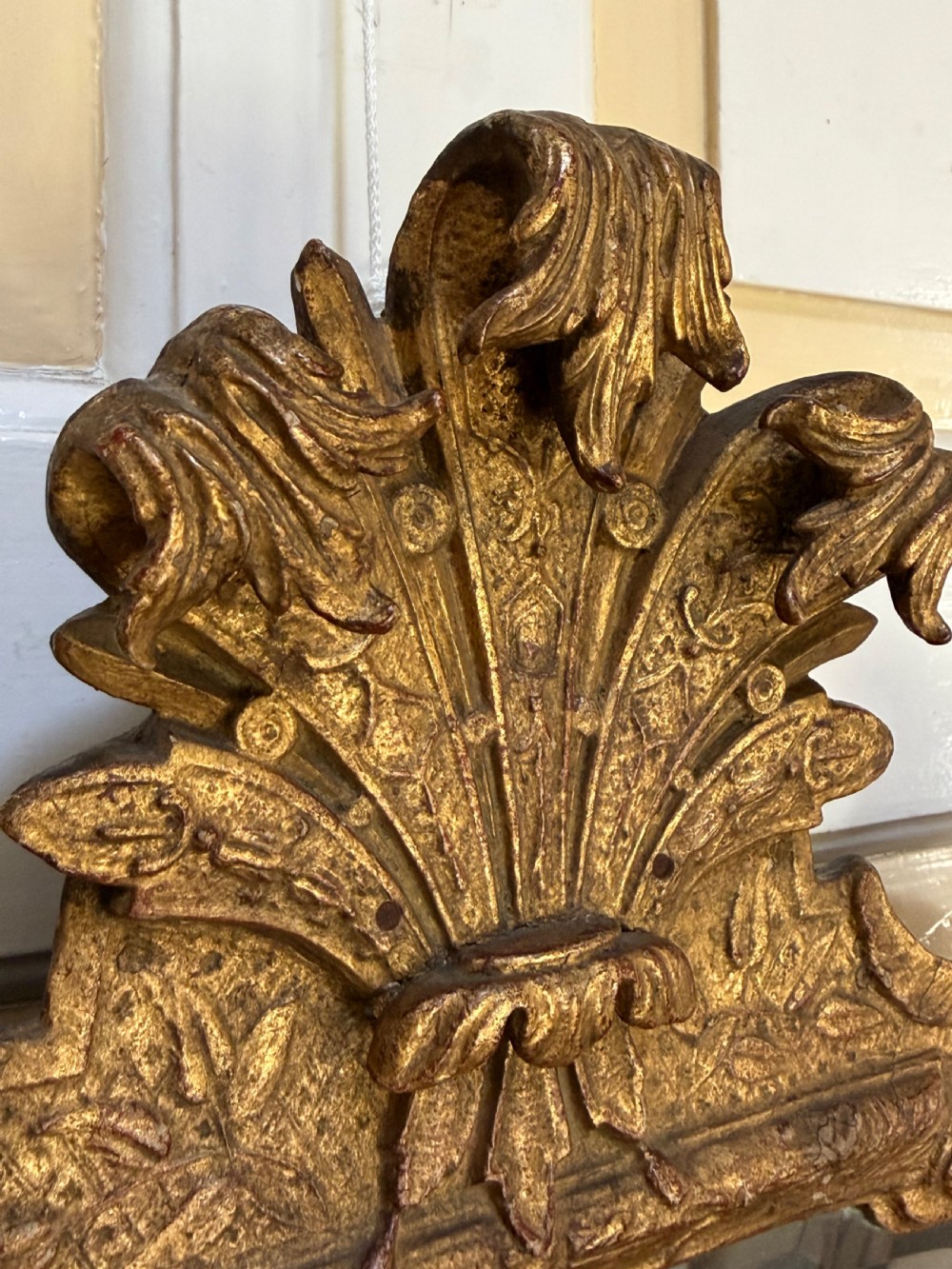 A tall, slender carved giltwood pier mirror featuring an ornate acanthus leaf cresting and an etched crest motif near the top of the glass plate. View XIII