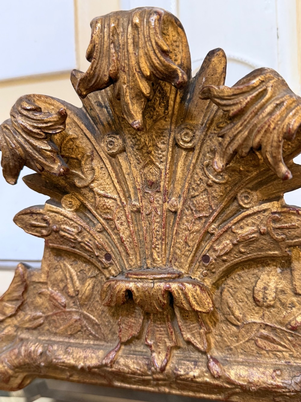 A tall, slender carved giltwood pier mirror featuring an ornate acanthus leaf cresting and an etched crest motif near the top of the glass plate. View XV