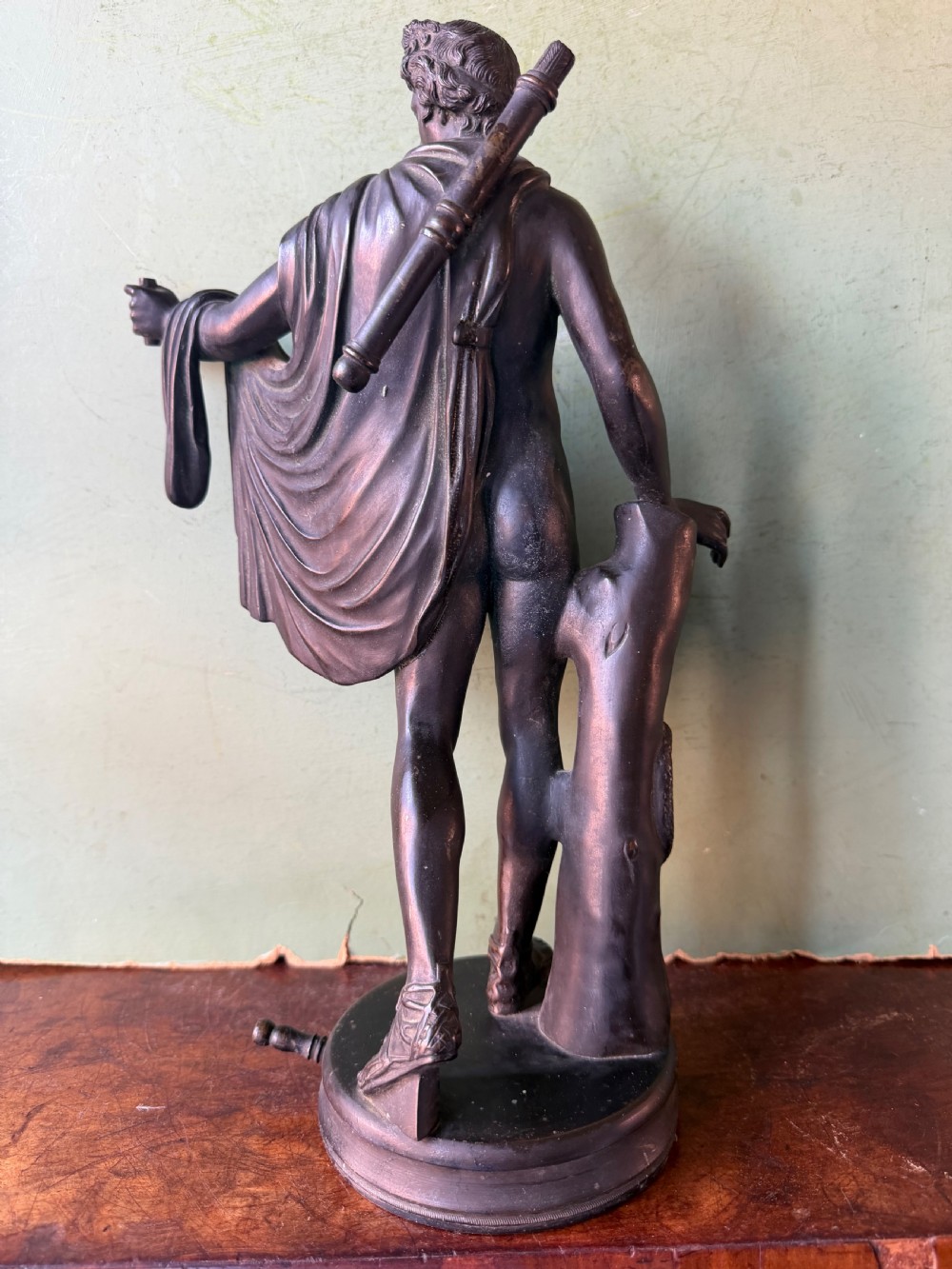 A dark patinated bronze figure depicting the classical god Apollo standing nude with drapery over his arm on a round base. View V
