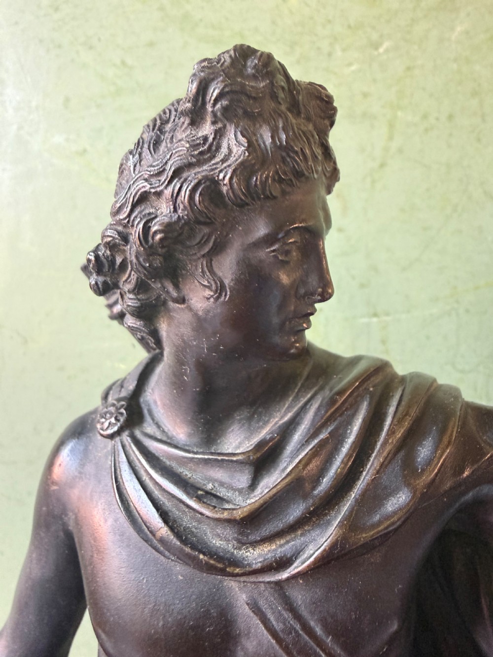 A dark patinated bronze figure depicting the classical god Apollo standing nude with drapery over his arm on a round base. View VII