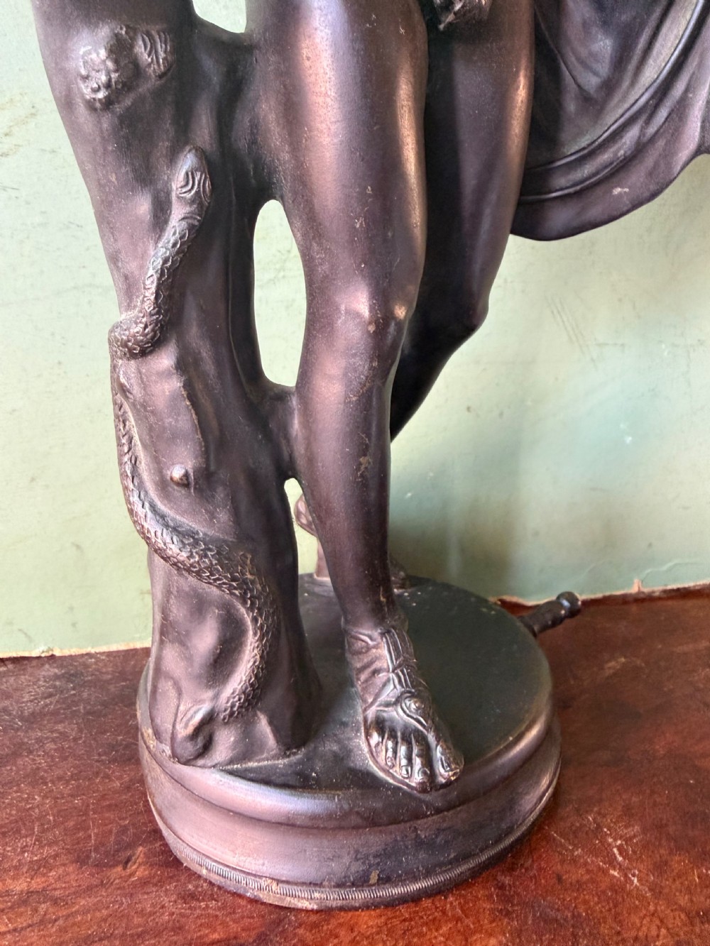 A dark patinated bronze figure depicting the classical god Apollo standing nude with drapery over his arm on a round base. View VIII