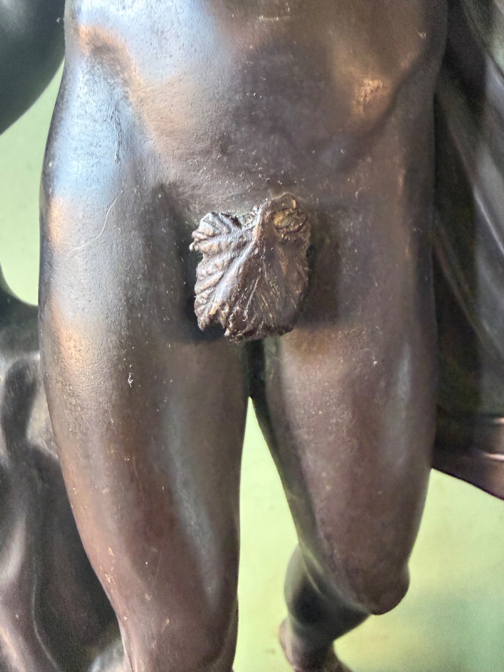 A dark patinated bronze figure depicting the classical god Apollo standing nude with drapery over his arm on a round base. View IX