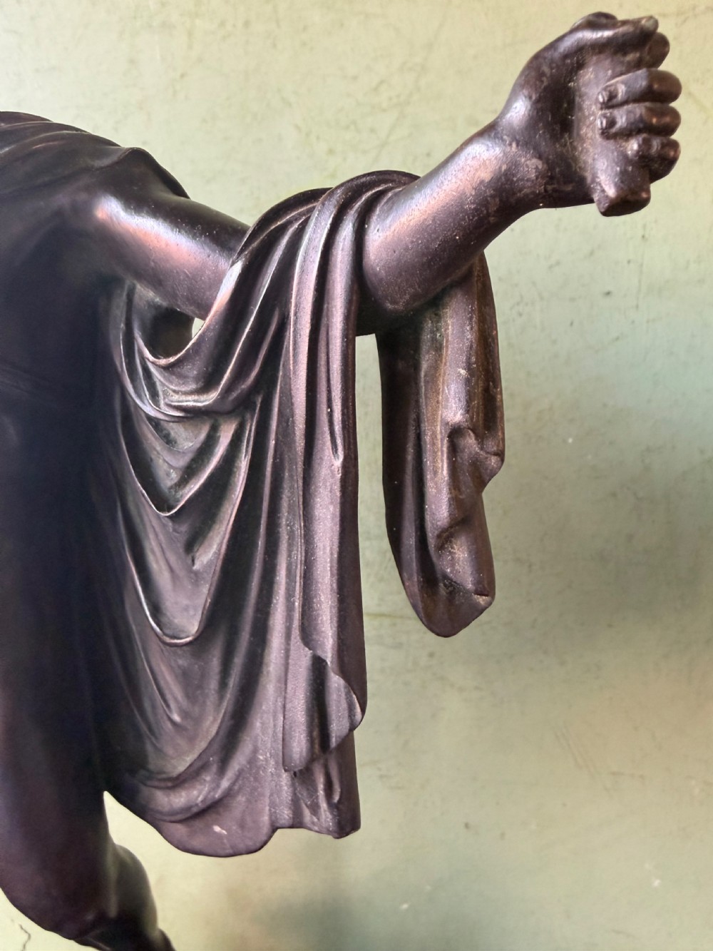 A dark patinated bronze figure depicting the classical god Apollo standing nude with drapery over his arm on a round base. View X