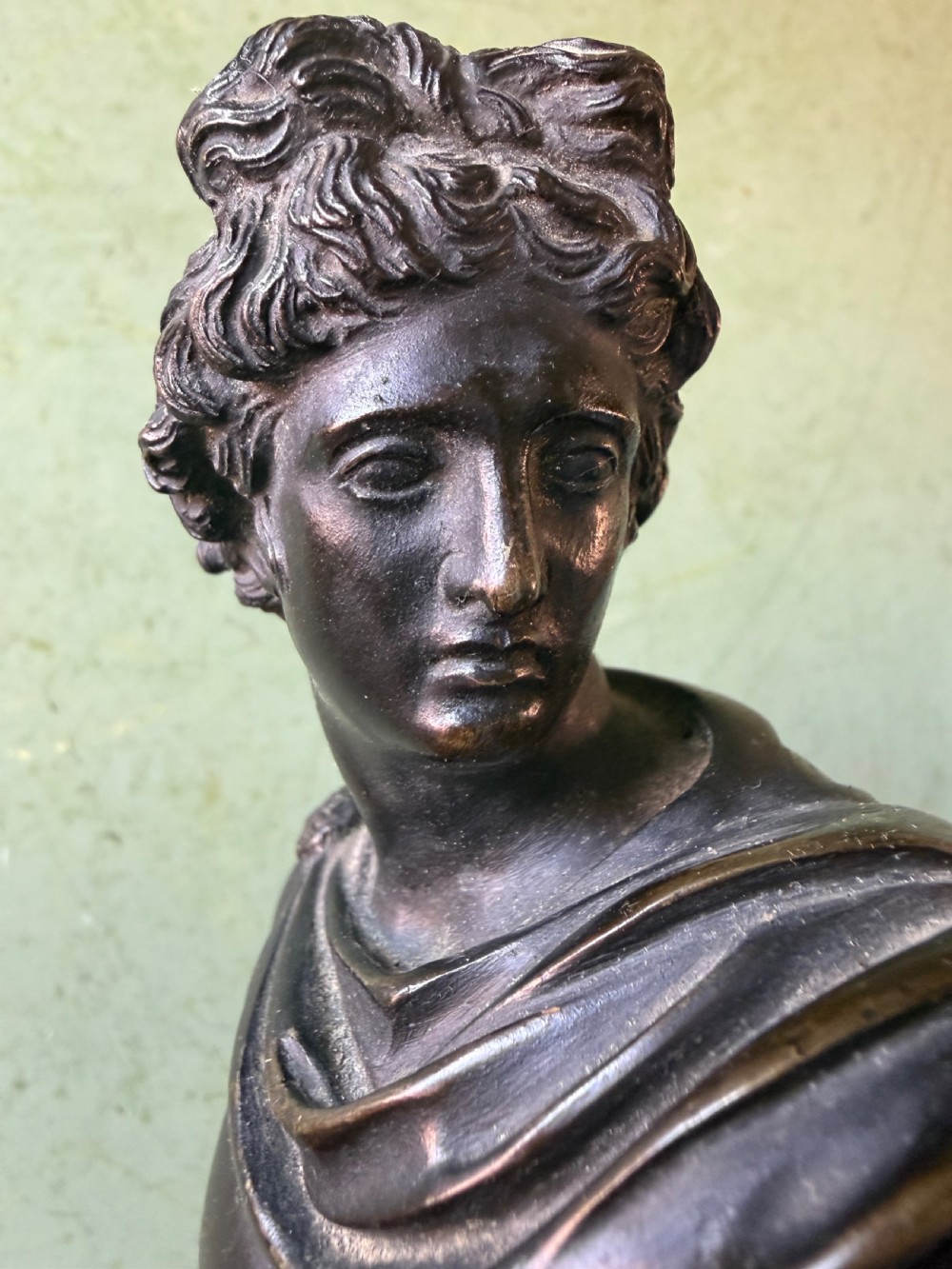 A dark patinated bronze figure depicting the classical god Apollo standing nude with drapery over his arm on a round base. View XI