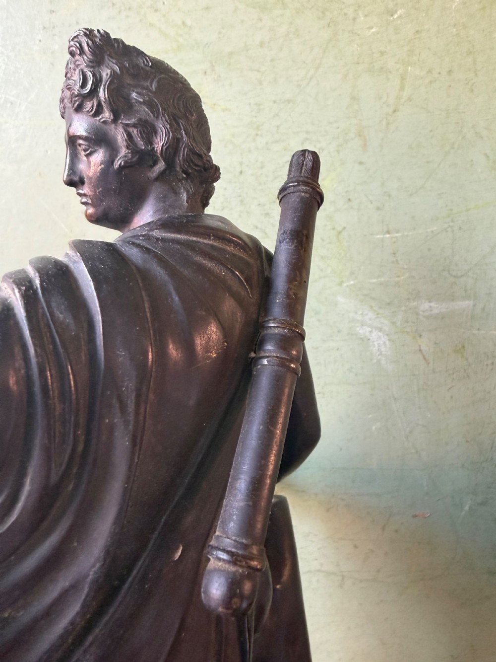 A dark patinated bronze figure depicting the classical god Apollo standing nude with drapery over his arm on a round base. View XII