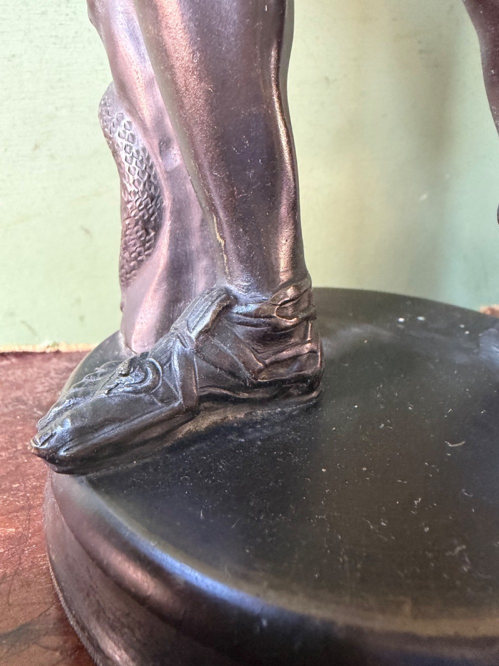 A dark patinated bronze figure depicting the classical god Apollo standing nude with drapery over his arm on a round base. View XIII
