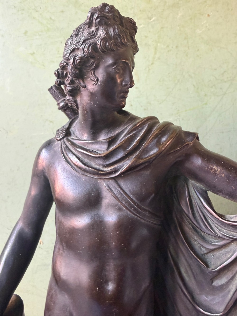 A dark patinated bronze figure depicting the classical god Apollo standing nude with drapery over his arm on a round base. View XVI