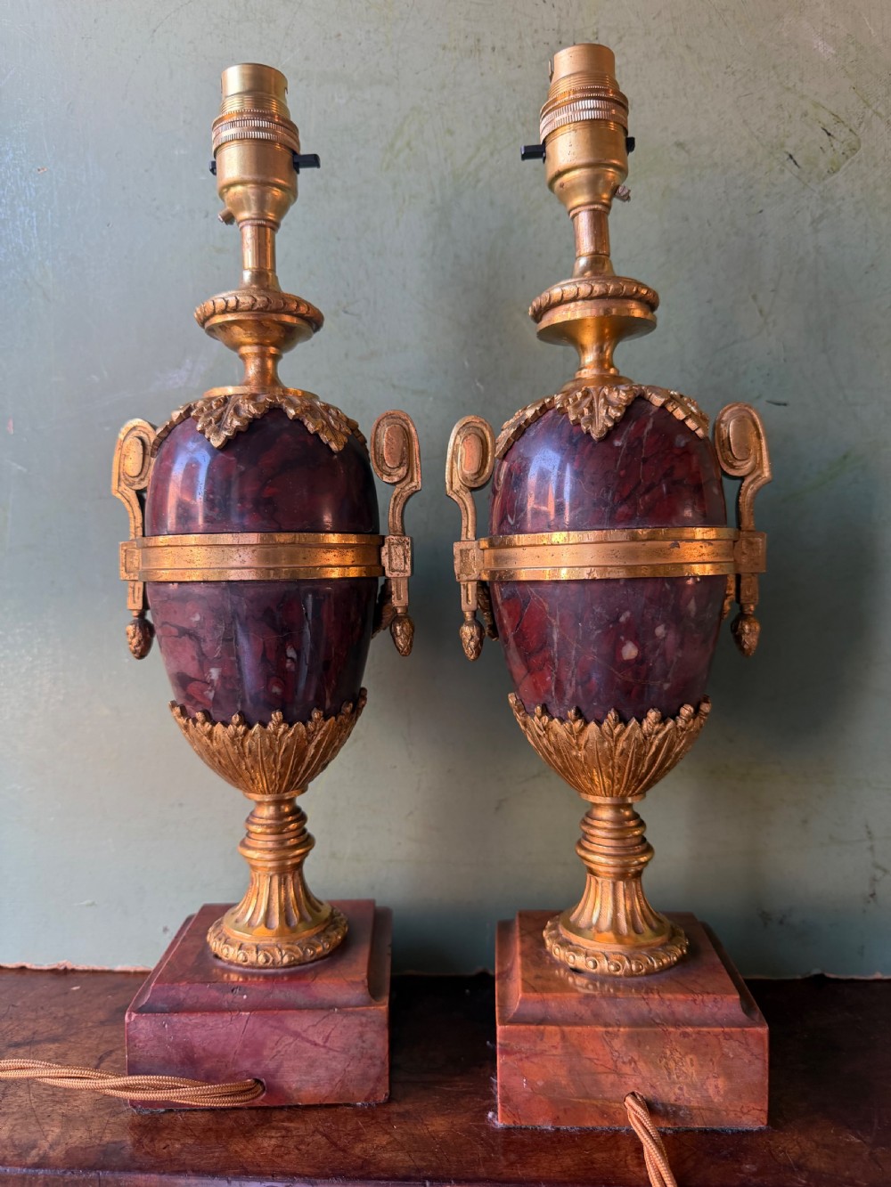 A pair of late nineteenth-century French rouge marble table lamps shaped as urns with gilt bronze mounts and square pedestal bases. View V