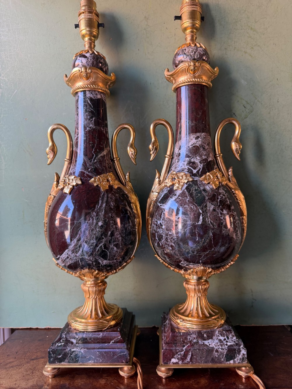 A pair of urn-shaped burgundy marble table lamps featuring gilded bronze swan handles and square pedestals. View IV