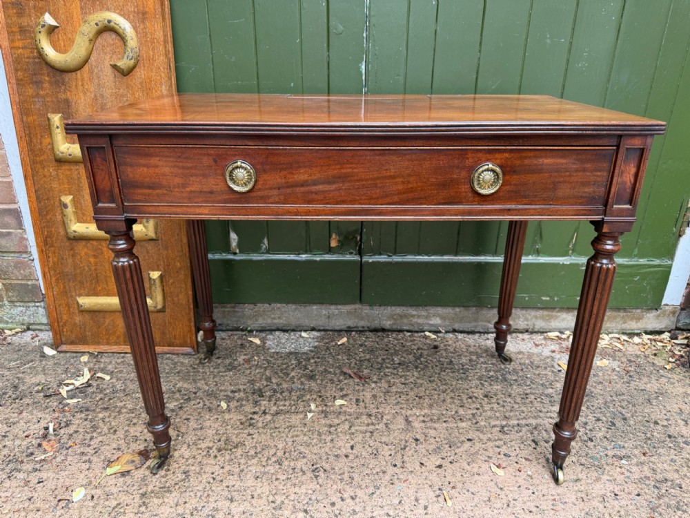 Early 19th-century George IV mahogany writing table featuring a long frieze drawer with brass rosette handles and reeded turned legs on castors. View II