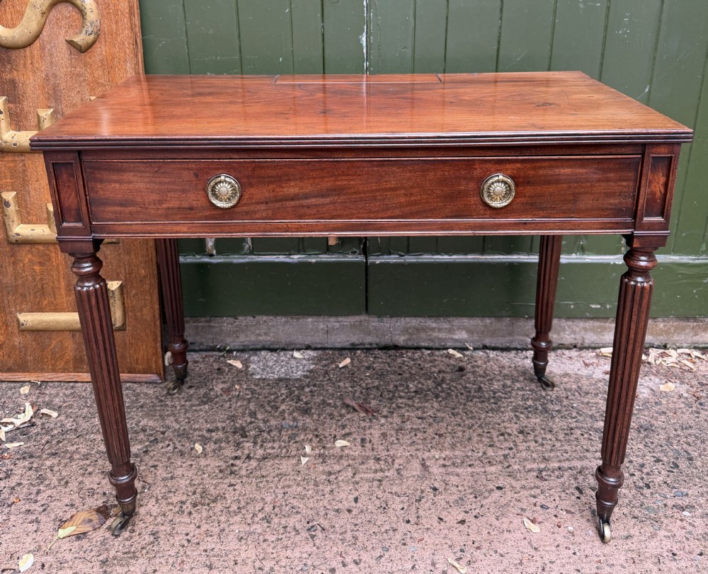 Early 19th-century George IV mahogany writing table featuring a long frieze drawer with brass rosette handles and reeded turned legs on castors.