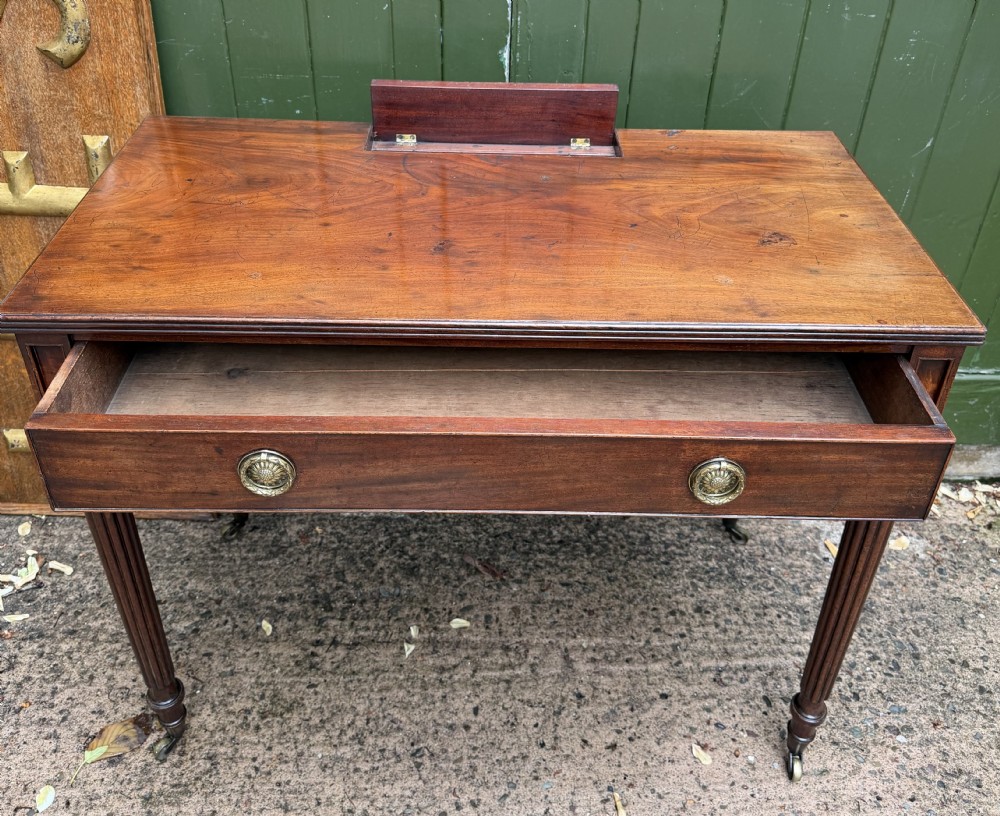 Early 19th-century George IV mahogany writing table featuring a long frieze drawer with brass rosette handles and reeded turned legs on castors. View III