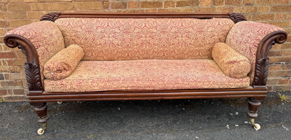 Early 19th-century William IV carved mahogany scroll-end sofa upholstered in red and gold patterned damask with matching bolster cushions.