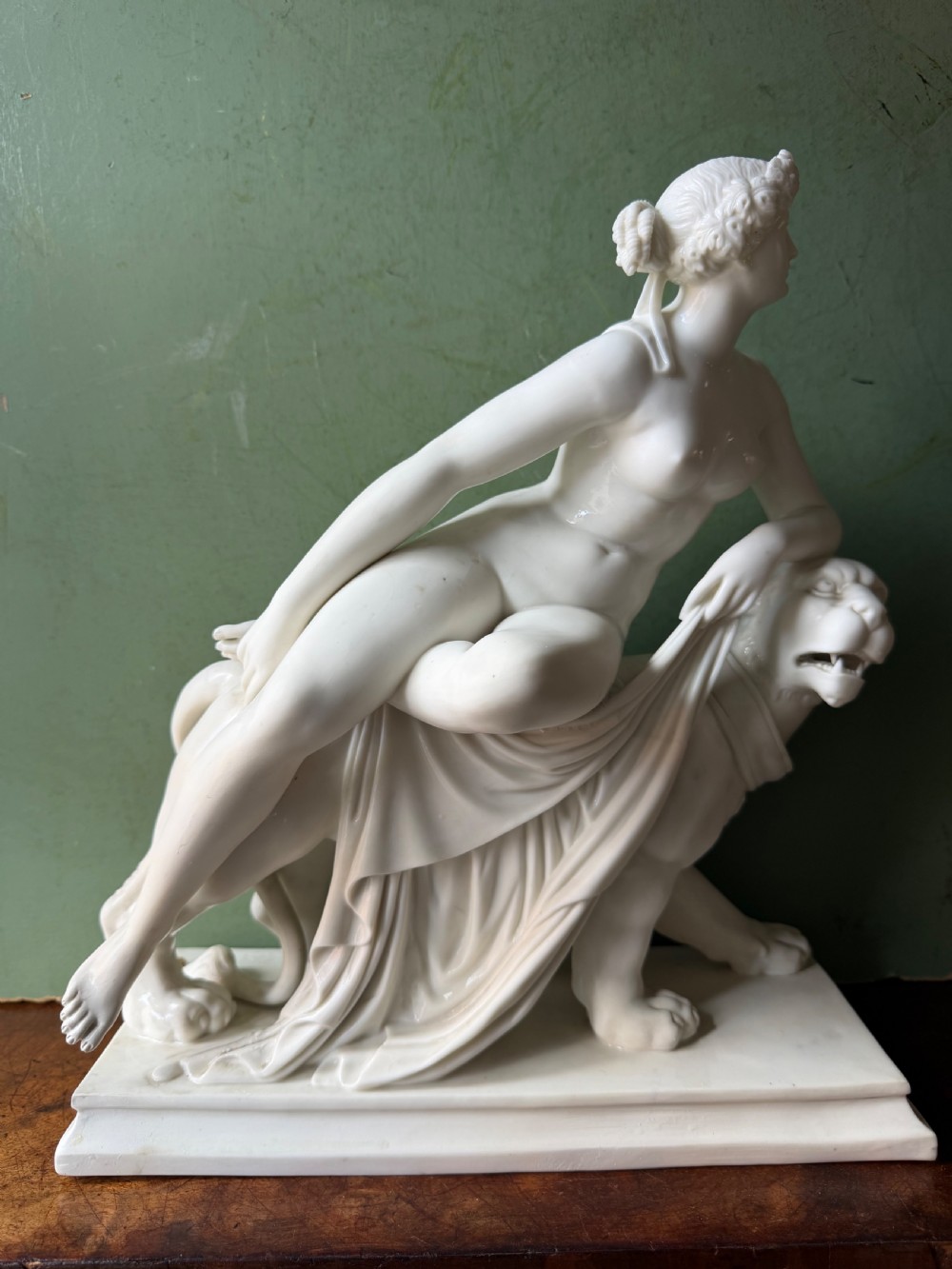 A white Parian porcelain Neoclassical sculpture depicting a reclining female figure mounted on the back of a panther on a rectangular plinth.