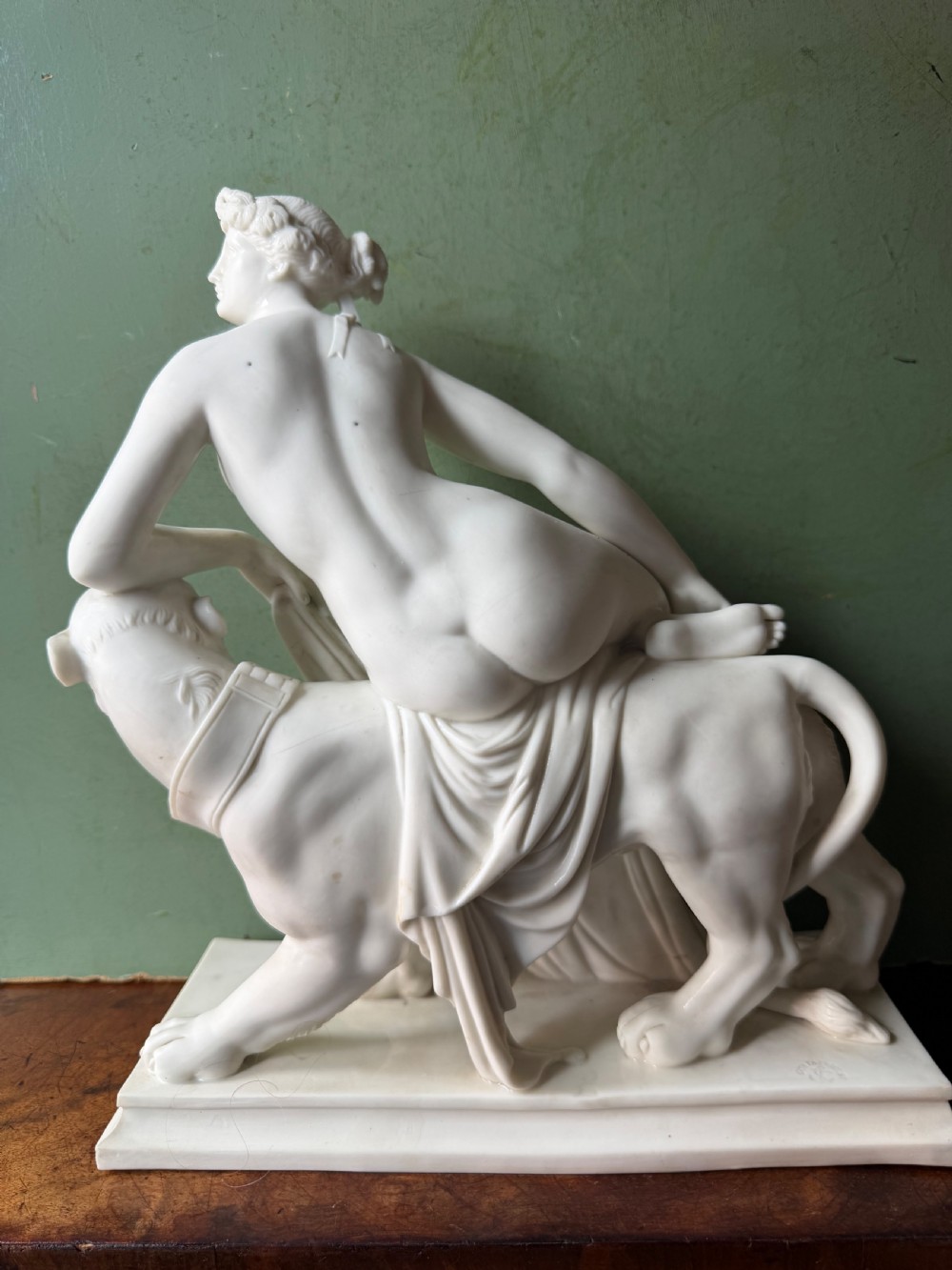 A white Parian porcelain Neoclassical sculpture depicting a reclining female figure mounted on the back of a panther on a rectangular plinth. View VII