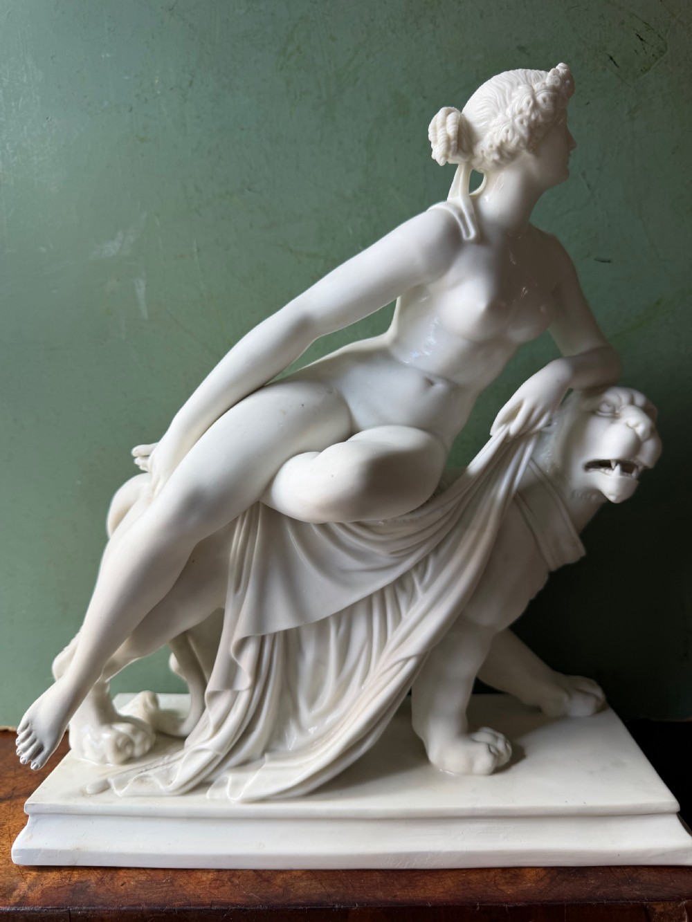 A white Parian porcelain Neoclassical sculpture depicting a reclining female figure mounted on the back of a panther on a rectangular plinth. View XIII