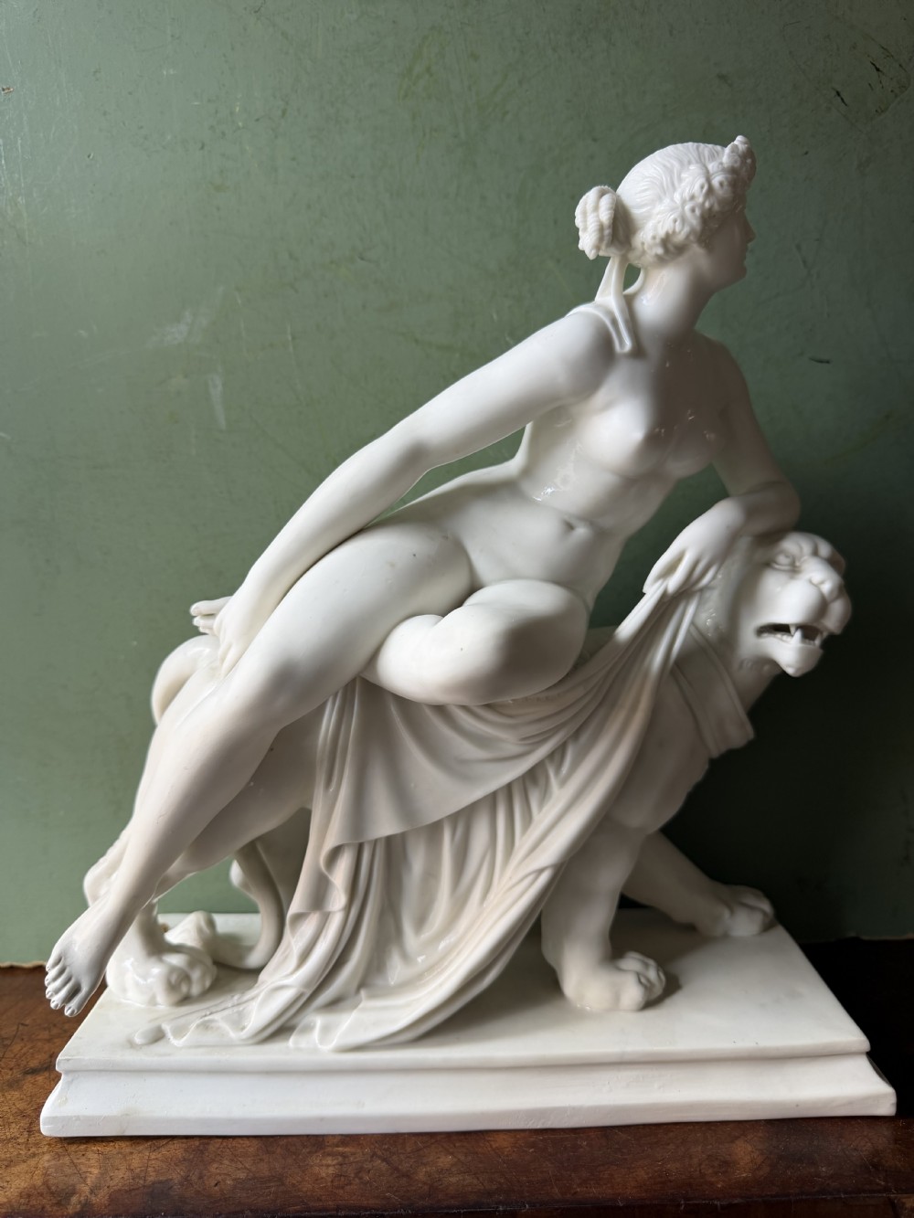 A white Parian porcelain Neoclassical sculpture depicting a reclining female figure mounted on the back of a panther on a rectangular plinth. View XVI