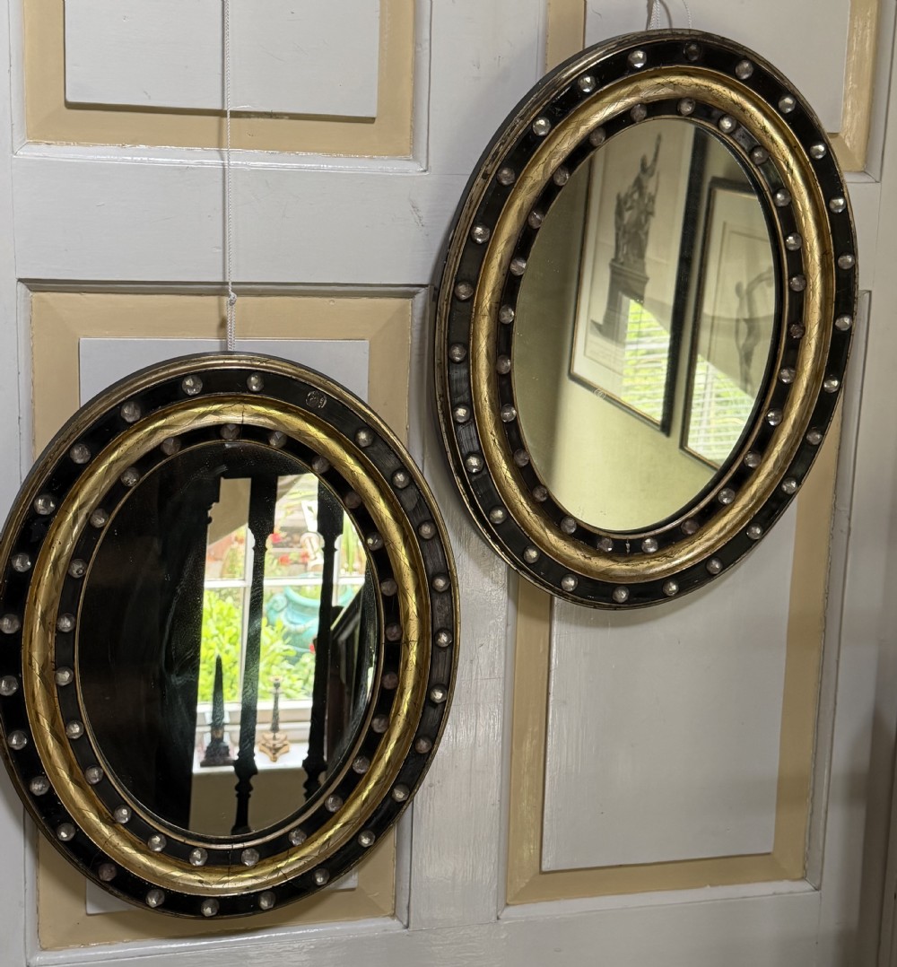 Scarce pair of early C19th Irish oval ebonised , parcel-gilt and glass cabochon mounted mirrors of smaller scale .