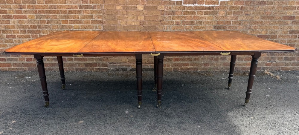 An early nineteenth-century Regency mahogany extending dining table featuring multiple drop-leaf sections and turned legs with brass castors. View II