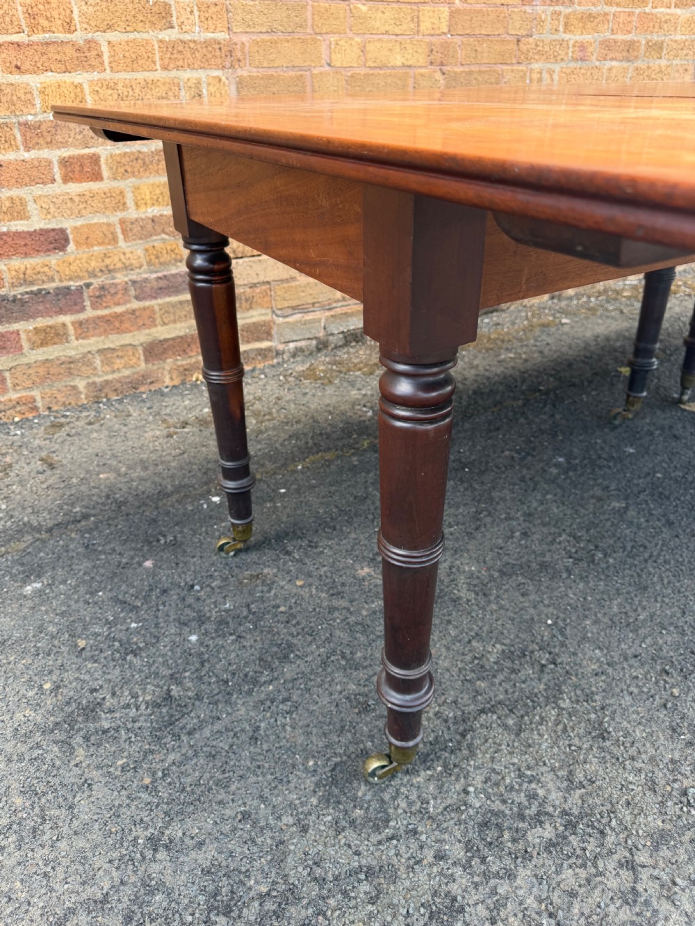 An early nineteenth-century Regency mahogany extending dining table featuring multiple drop-leaf sections and turned legs with brass castors. View VIII