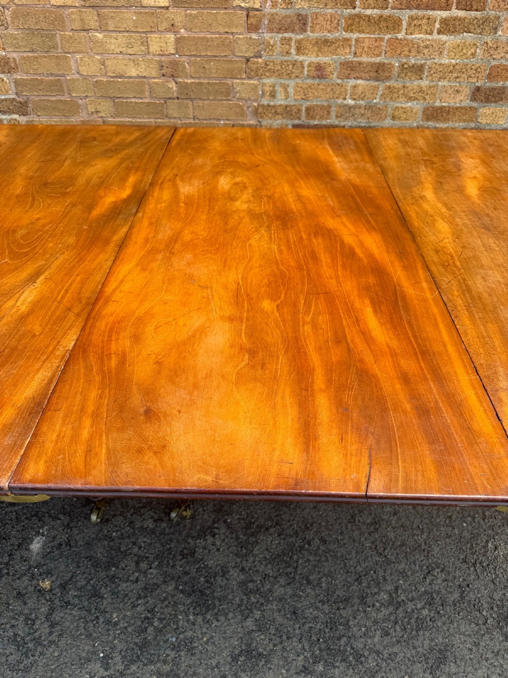 An early nineteenth-century Regency mahogany extending dining table featuring multiple drop-leaf sections and turned legs with brass castors. View XI