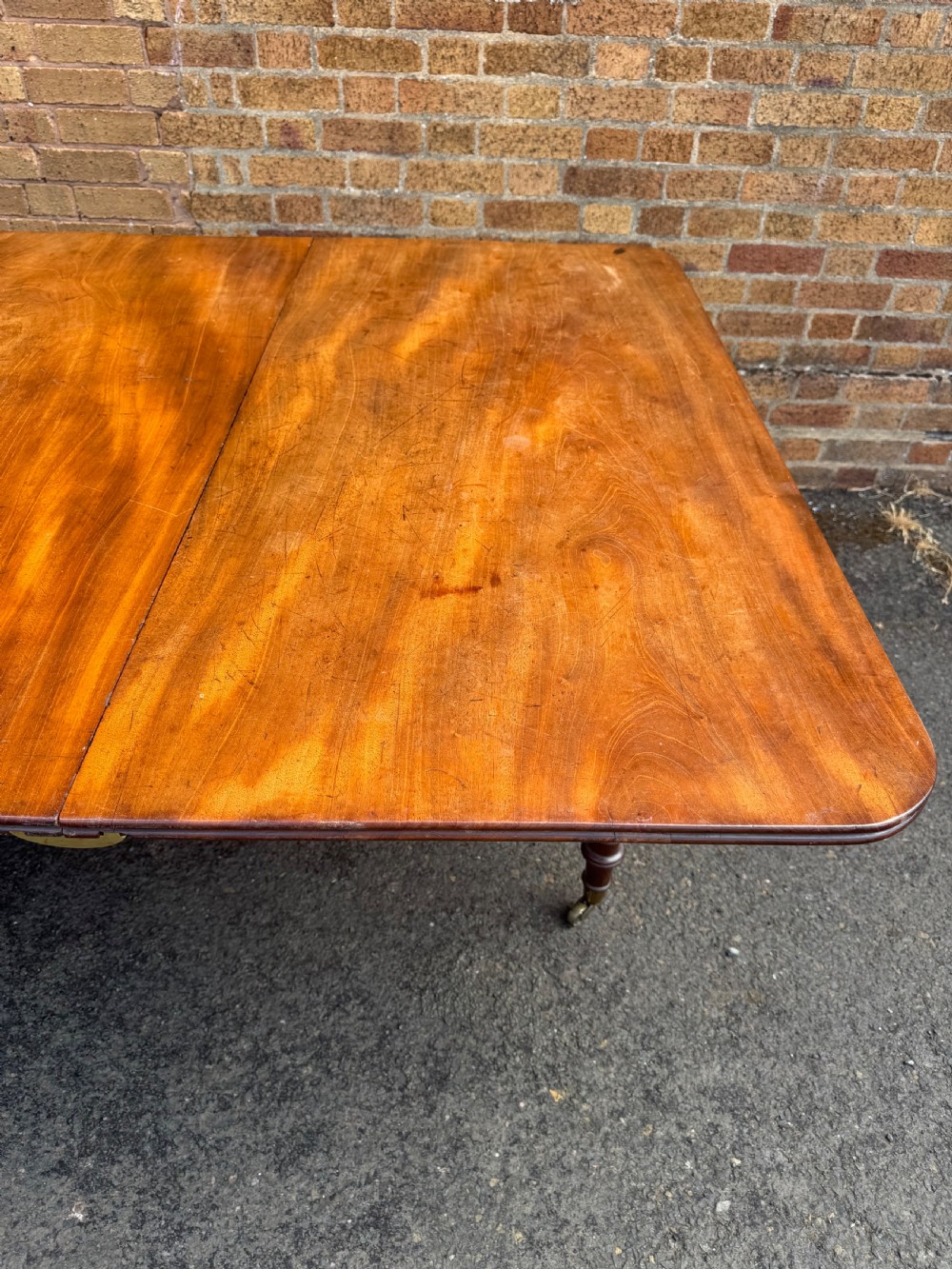 An early nineteenth-century Regency mahogany extending dining table featuring multiple drop-leaf sections and turned legs with brass castors. View XII