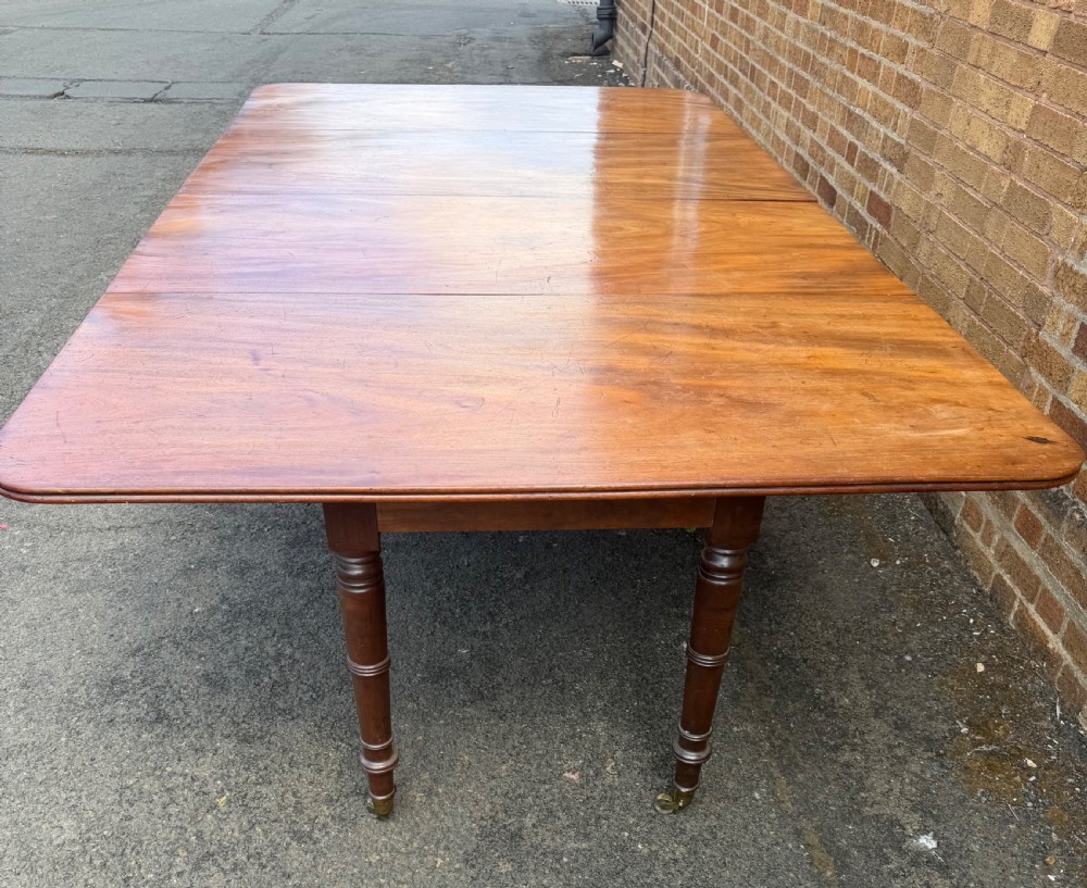 An early nineteenth-century Regency mahogany extending dining table featuring multiple drop-leaf sections and turned legs with brass castors. View XIII