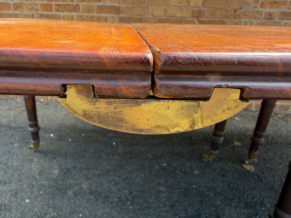 An early nineteenth-century Regency mahogany extending dining table featuring multiple drop-leaf sections and turned legs with brass castors. View XV
