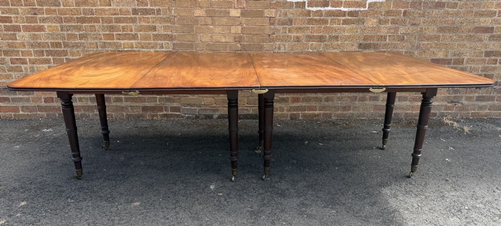 An early nineteenth-century Regency mahogany extending dining table featuring multiple drop-leaf sections and turned legs with brass castors. View III