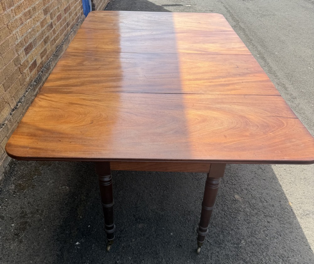 An early nineteenth-century Regency mahogany extending dining table featuring multiple drop-leaf sections and turned legs with brass castors. View IV