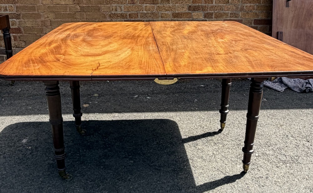 An early nineteenth-century Regency mahogany extending dining table featuring multiple drop-leaf sections and turned legs with brass castors. View VII