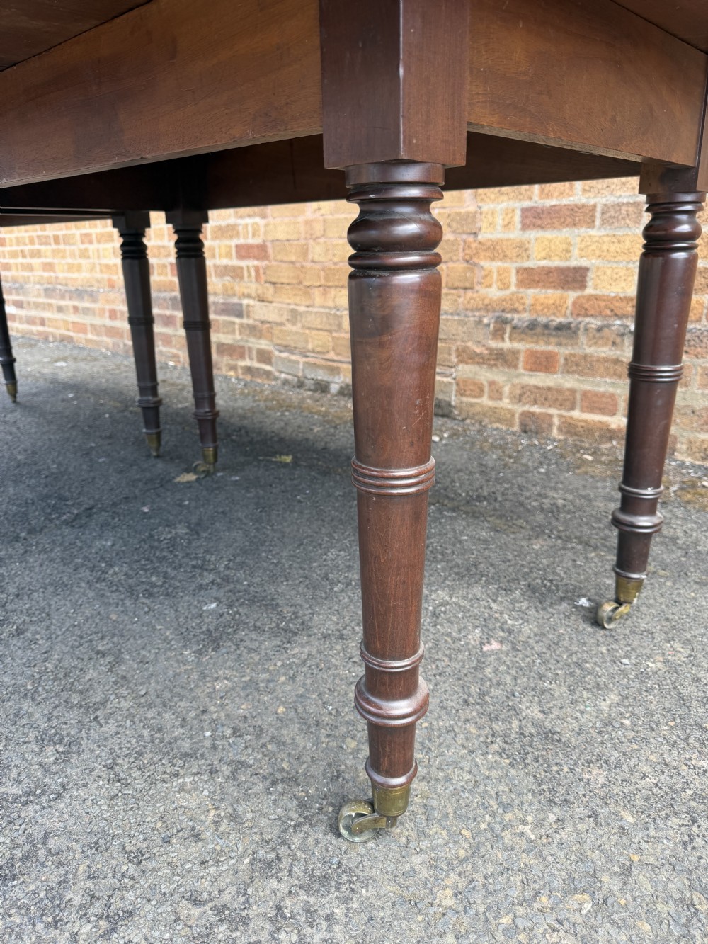 An early nineteenth-century Regency mahogany extending dining table featuring multiple drop-leaf sections and turned legs with brass castors. View XXIX