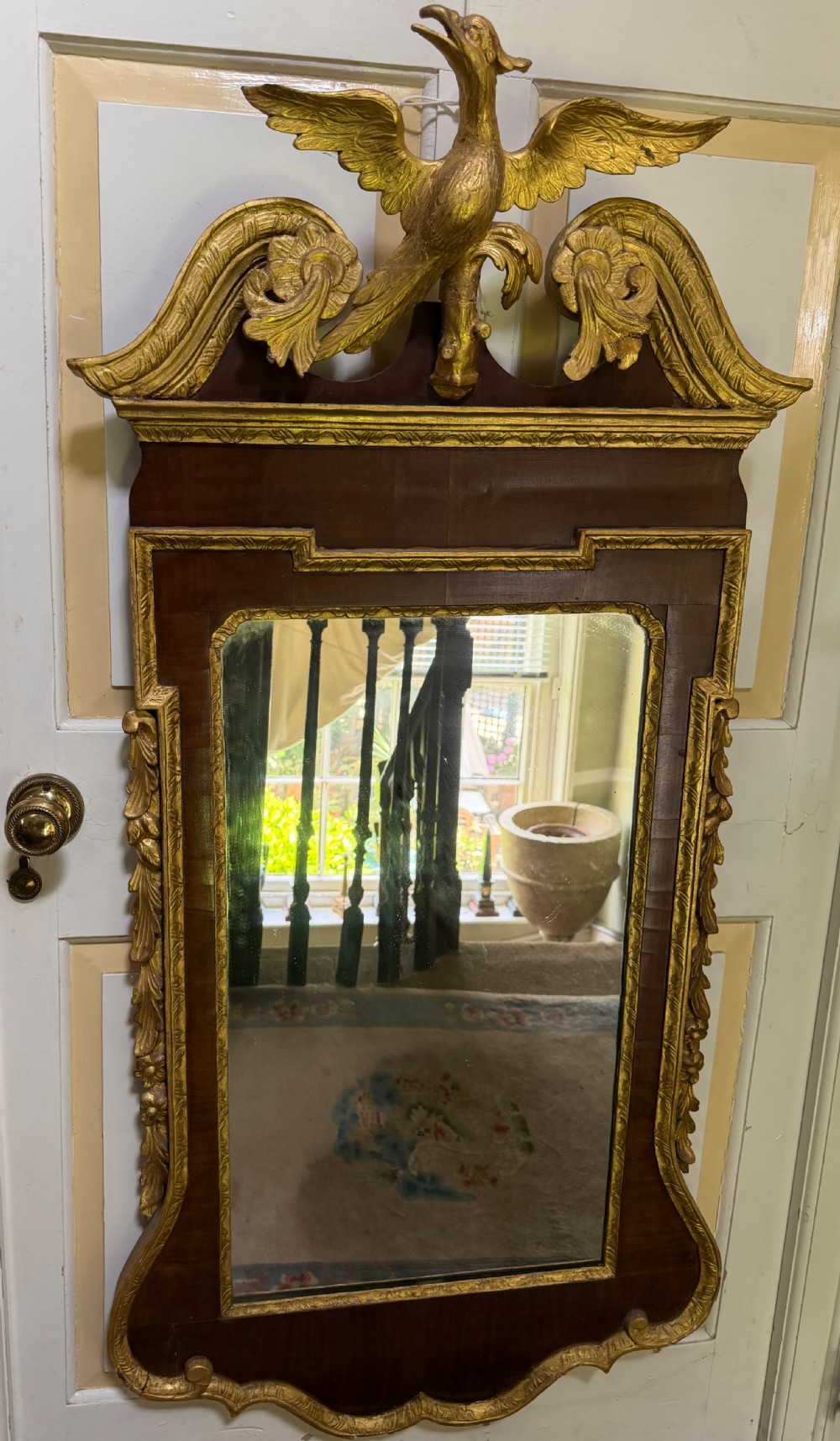 A nineteenth-century George II revival mahogany pier mirror featuring parcel-gilt mouldings, side foliage carvings, a broken pediment, and a carved eagle finial.