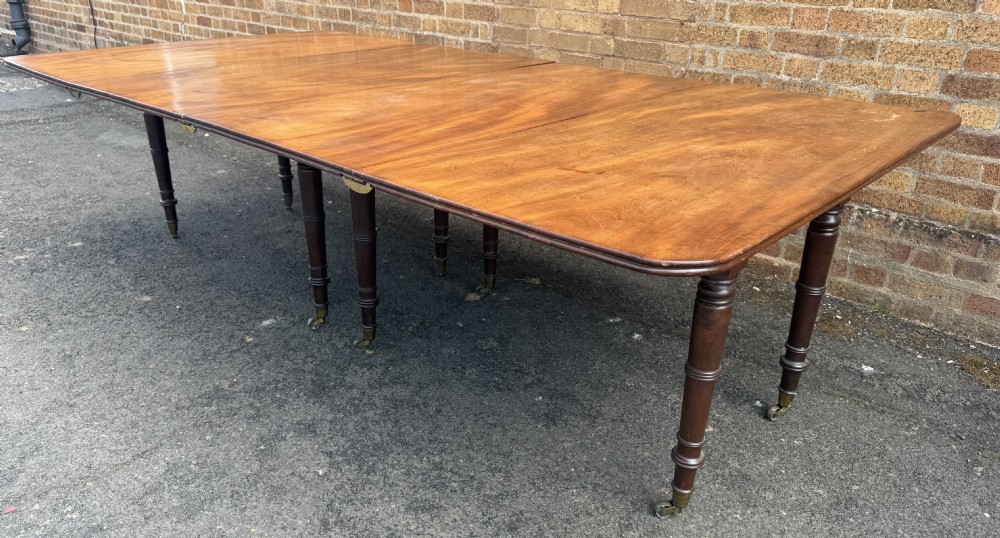 An early nineteenth-century Regency mahogany extending dining table featuring multiple drop-leaf sections and turned legs with brass castors. View XXX