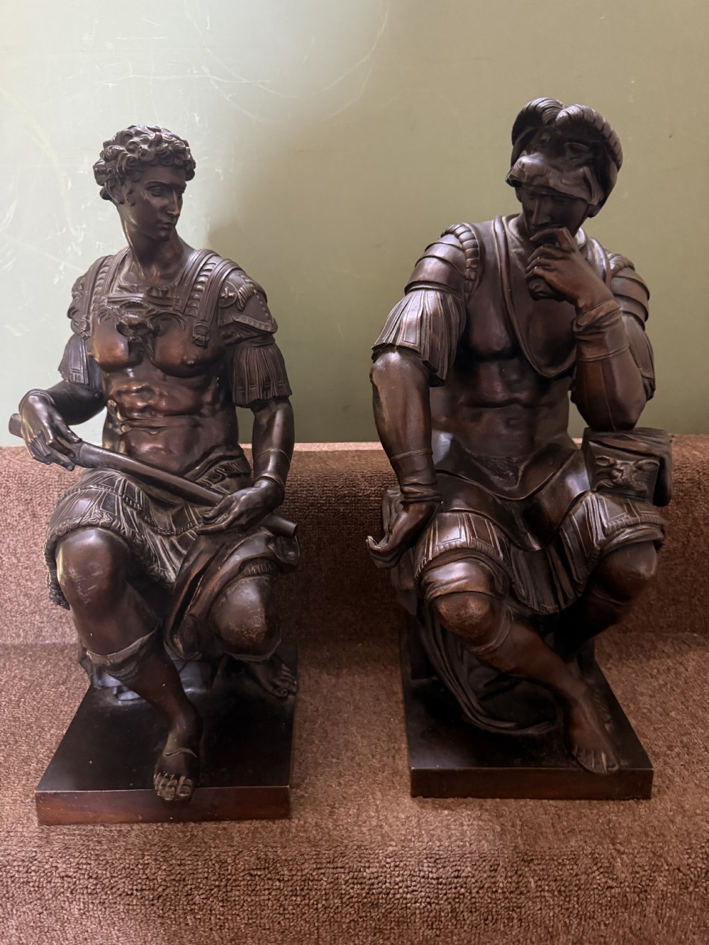 A pair of patinated dark bronze sculptures depicting two seated male figures in classical Roman armour mounted on rectangular bases. View XVIII