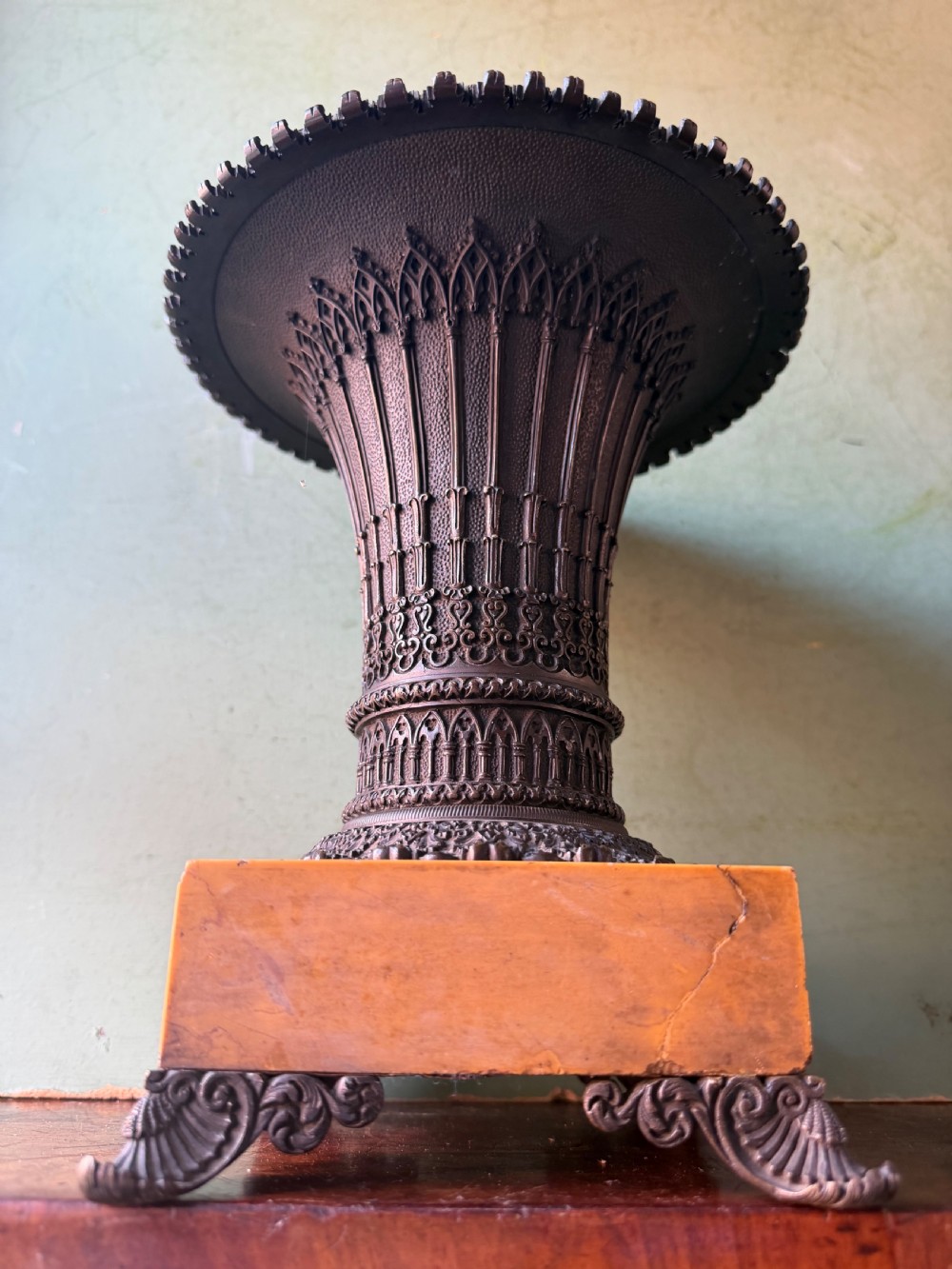 A pair of early nineteenth-century French bronze flared urns with Gothic tracery detailing, set upon square yellow Siena marble plinth bases with bronze bracket feet. View V