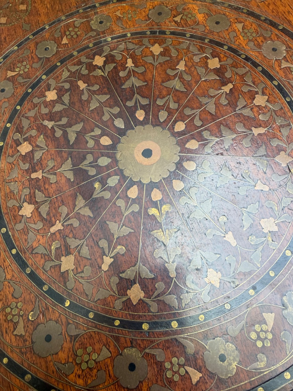 An octagonal Anglo-Indian teak side table featuring intricate floral and geometric brass and copper wire inlay on its top surface, set upon a carved and pierced folding lattice wooden base. View IV