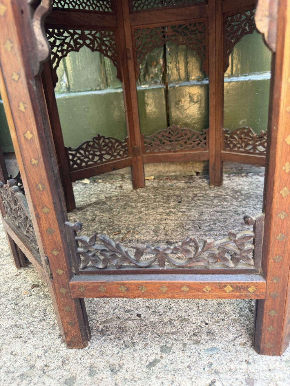 An octagonal Anglo-Indian teak side table featuring intricate floral and geometric brass and copper wire inlay on its top surface, set upon a carved and pierced folding lattice wooden base. View VIII