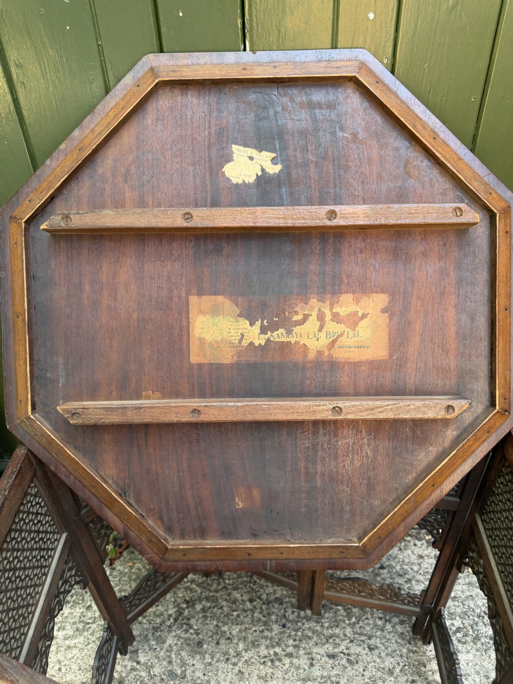 An octagonal Anglo-Indian teak side table featuring intricate floral and geometric brass and copper wire inlay on its top surface, set upon a carved and pierced folding lattice wooden base. View XIX