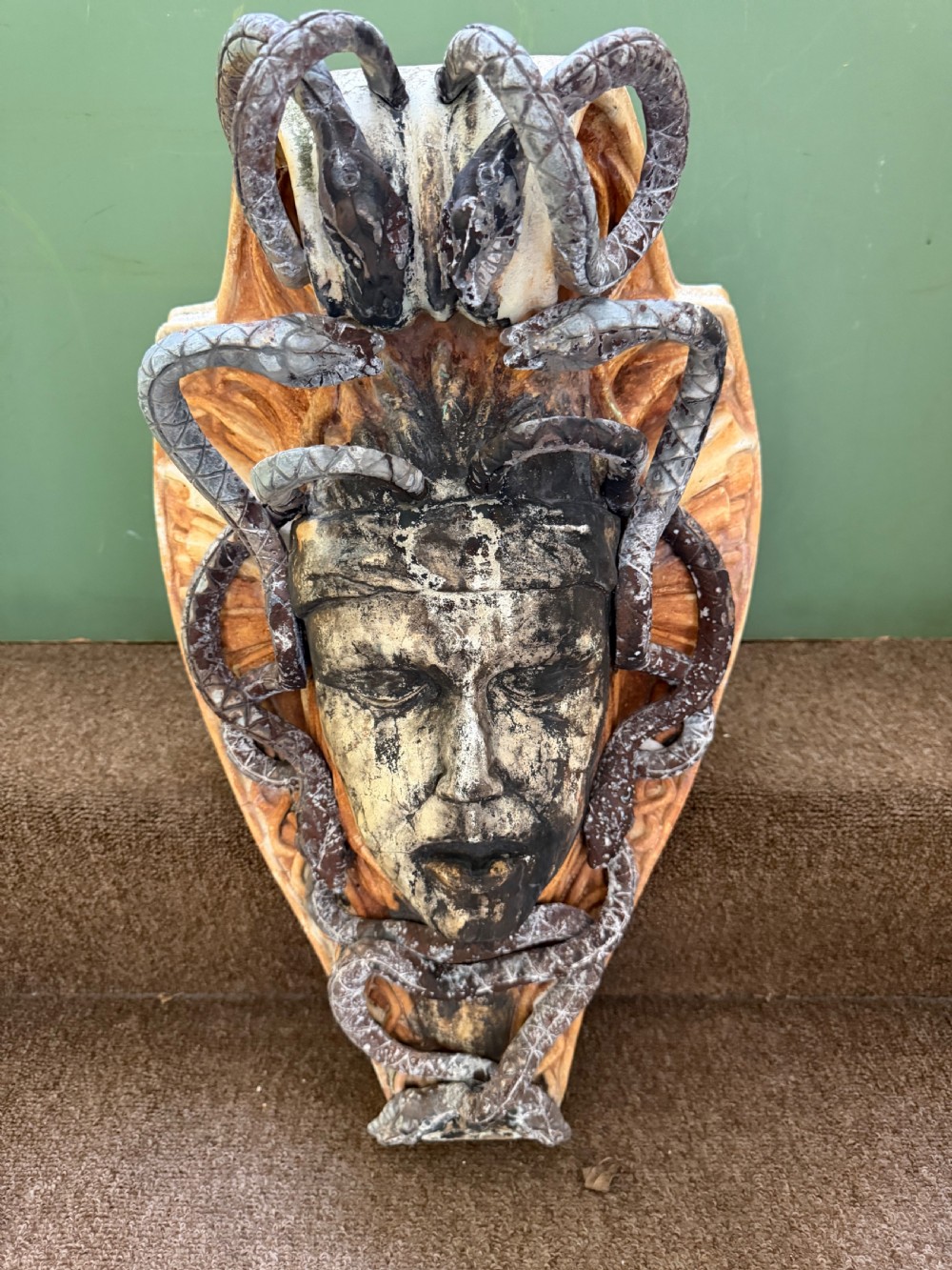 A carved stone wall bracket featuring a central Medusa head motif surrounded by lead-formed serpents against an arched background.