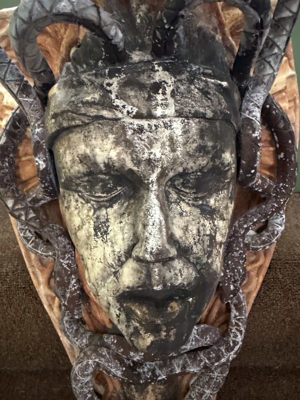 A carved stone wall bracket featuring a central Medusa head motif surrounded by lead-formed serpents against an arched background. View V