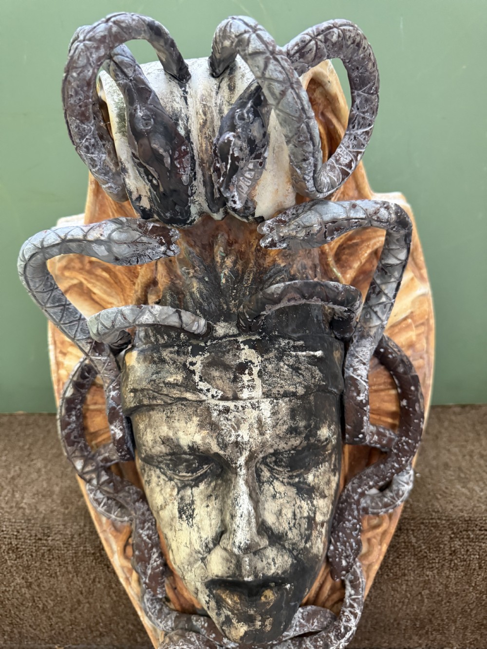 A carved stone wall bracket featuring a central Medusa head motif surrounded by lead-formed serpents against an arched background. View IX